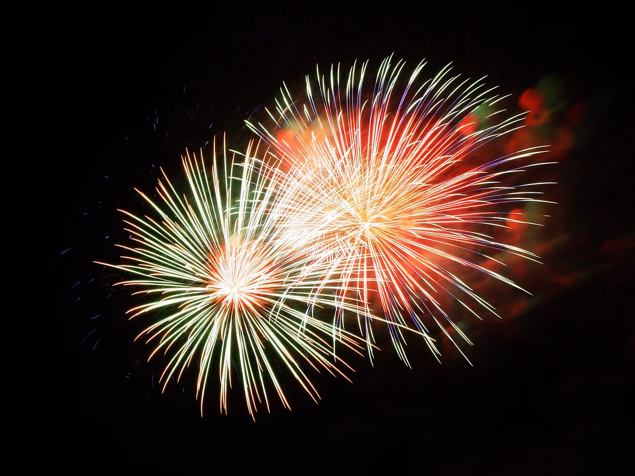 Two large colorful fireworks exploding against a black night sky backdrop.