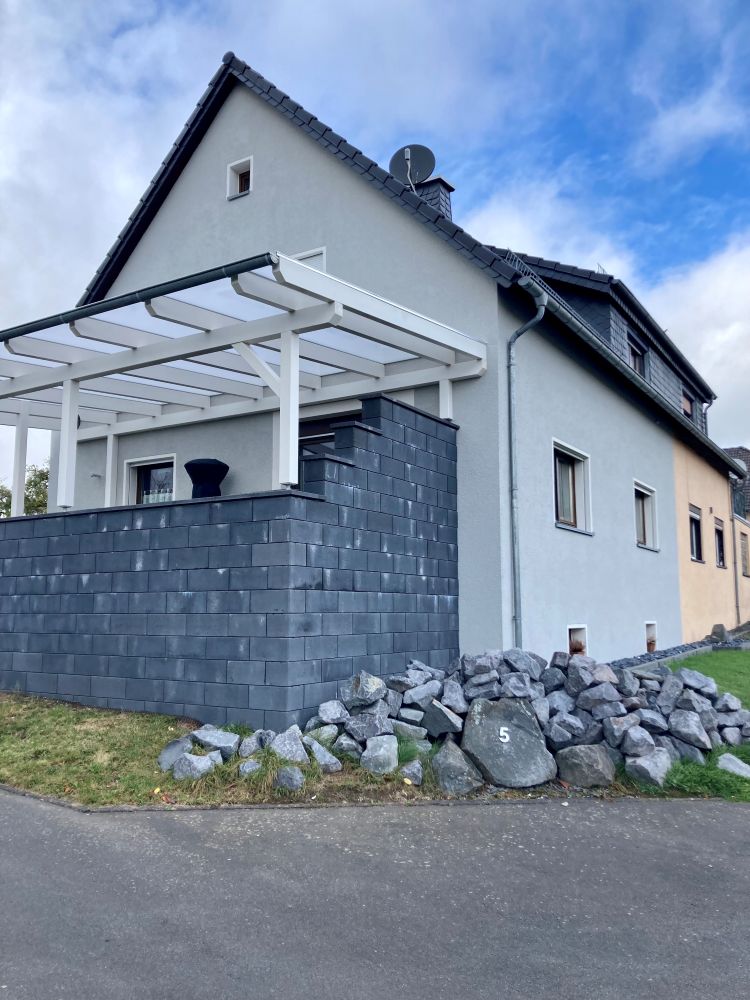 Wohnhaus mit verputzter Fassade, überdachter und mit Steinen abgegrenzter Terrasse