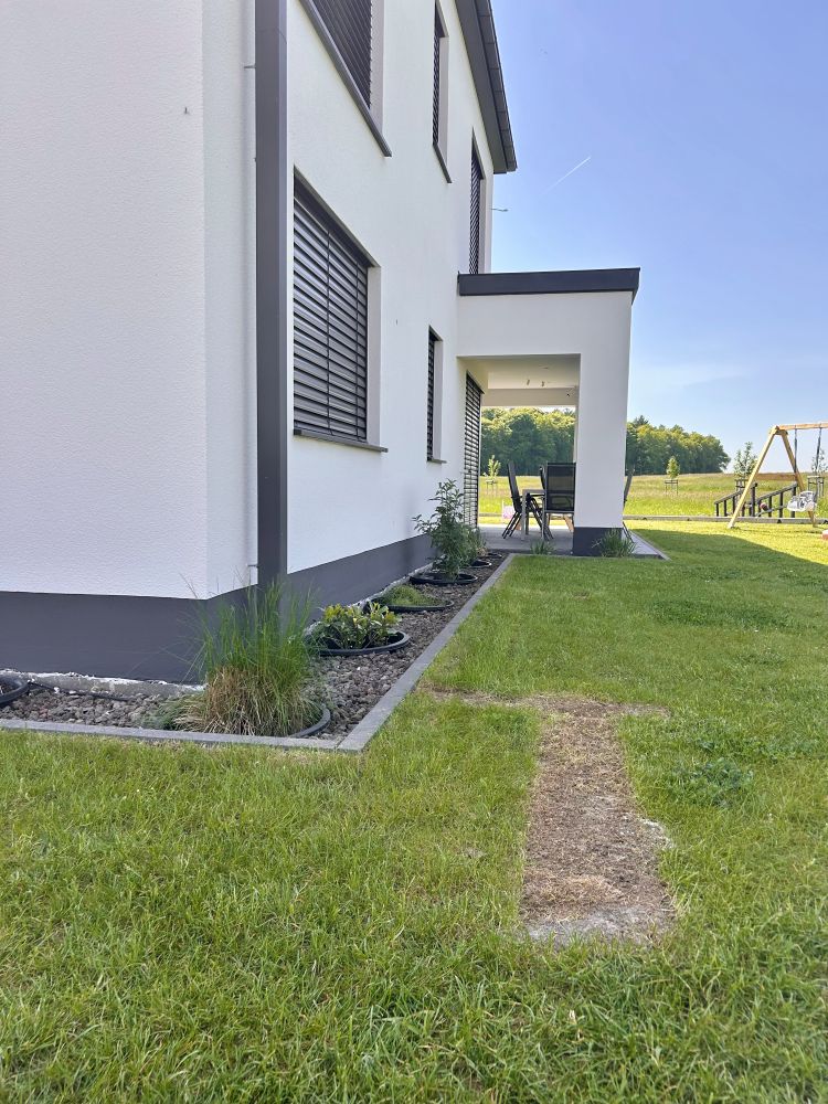 Einfamilienhaus von außen mit weißer Fassade, gemähter Wiese