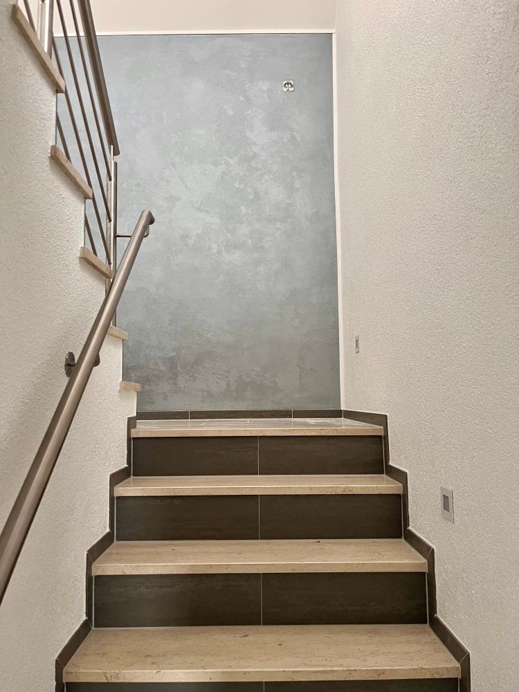 Treppenansicht von Innen eines Hauses mit Geländer und einer grau gestrichenen Wand