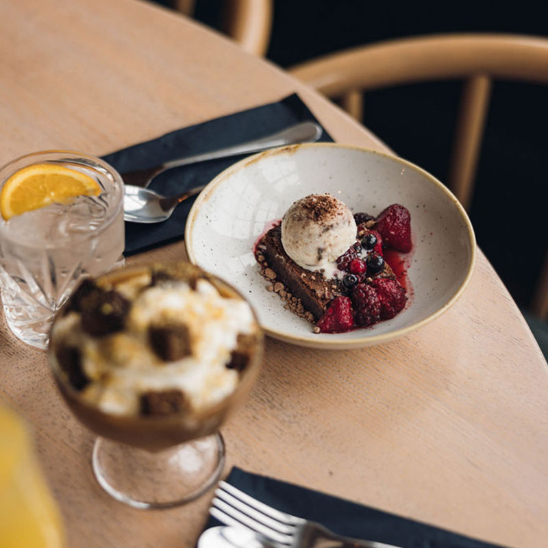 Plate with chocolate dessert topped with a scoop of vanilla ice cream and surrounded by fresh raspberries and blueberries on a wooden table with a glass of water with lemon.