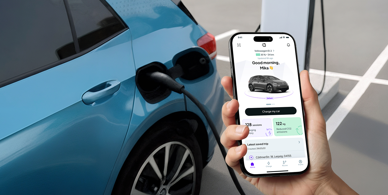 Hand holding smartphone displaying a car charging app next to a blue electric vehicle being charged.