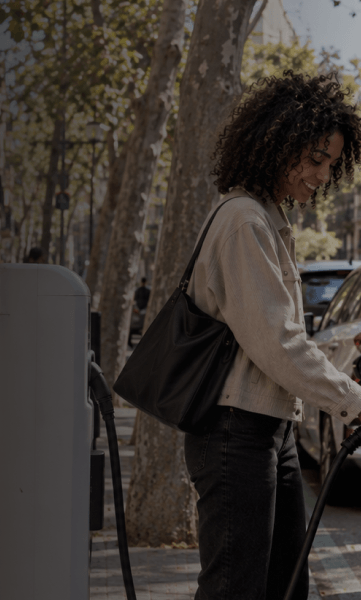 Smiling woman holding an electric vehicle charger outdoors against a clear sky background.