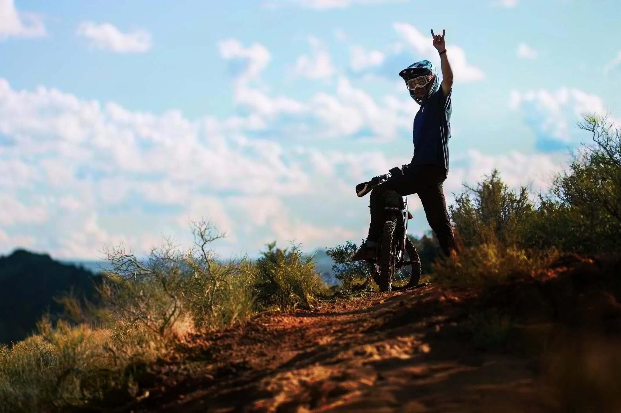 Rider on a surron rental electric dirt bike on a trail giving a rock-on hand gesture