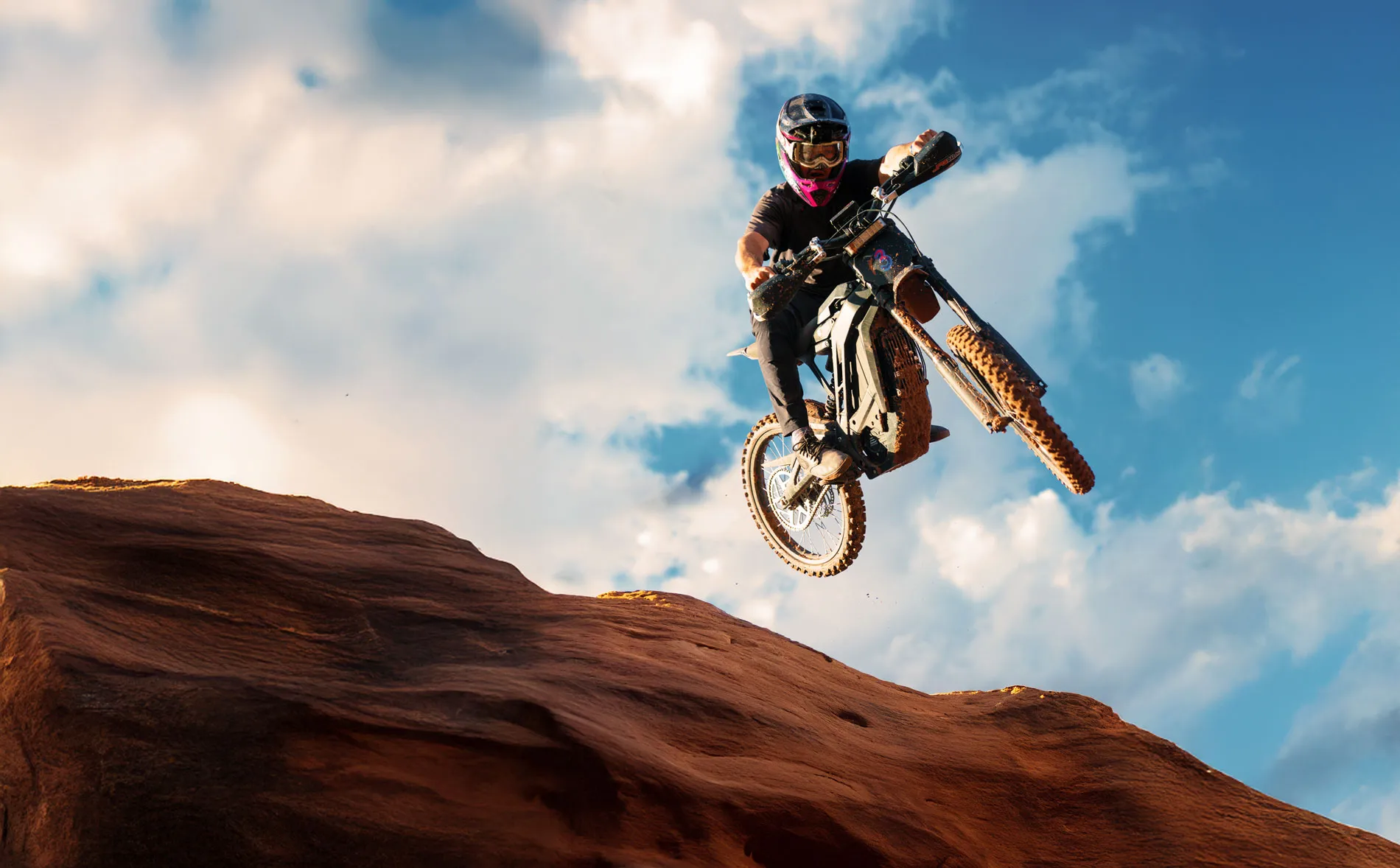 Three surron riders on dirt bikes racing on a muddy dirt trail in a natural outdoor setting with one rider kicking up mud.