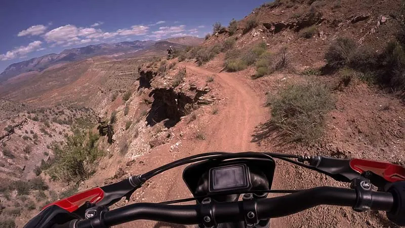 View from a dirt bike on a narrow single-track dirt trail winding along a steep rocky mountain with another motorcyclist ahead, Toquerville Twister Southern Utah.