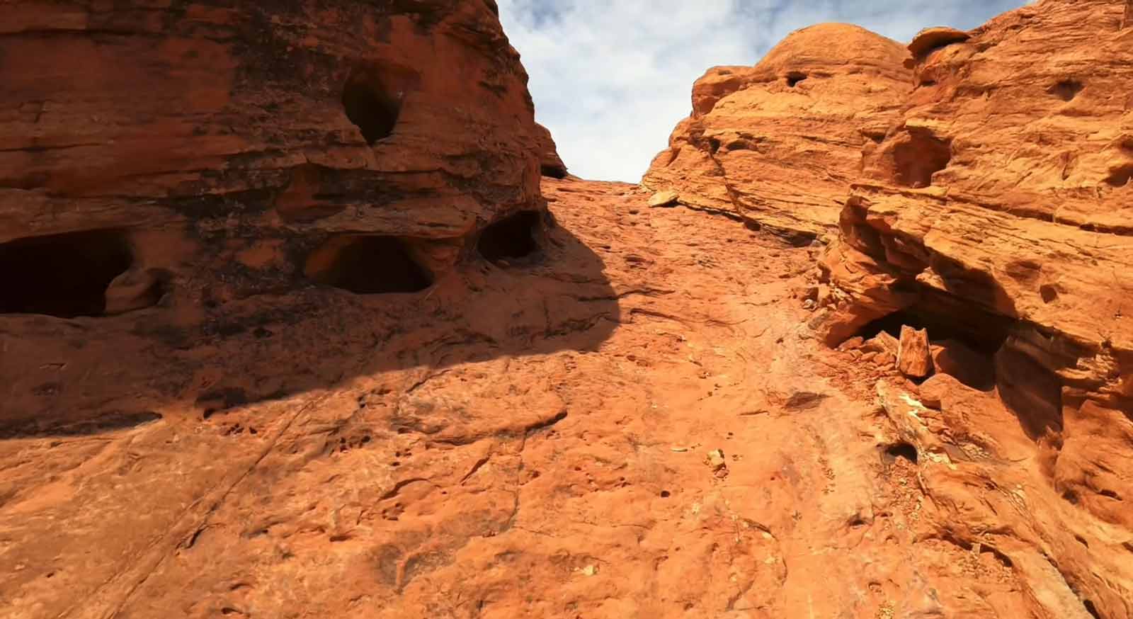 Red sandstone rock formations with multiple small caves under a partly cloudy sky dirt bike trail Southern Utah.