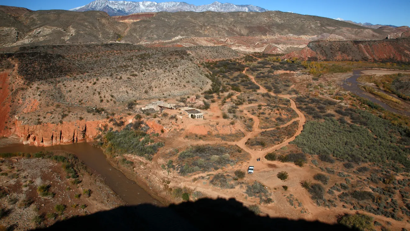 Aerial view of rugged desert landscape with dirt trails, scattered bushes, a winding river, and snow-capped mountains in the background Babylon Virgin River, Southern Utah.
