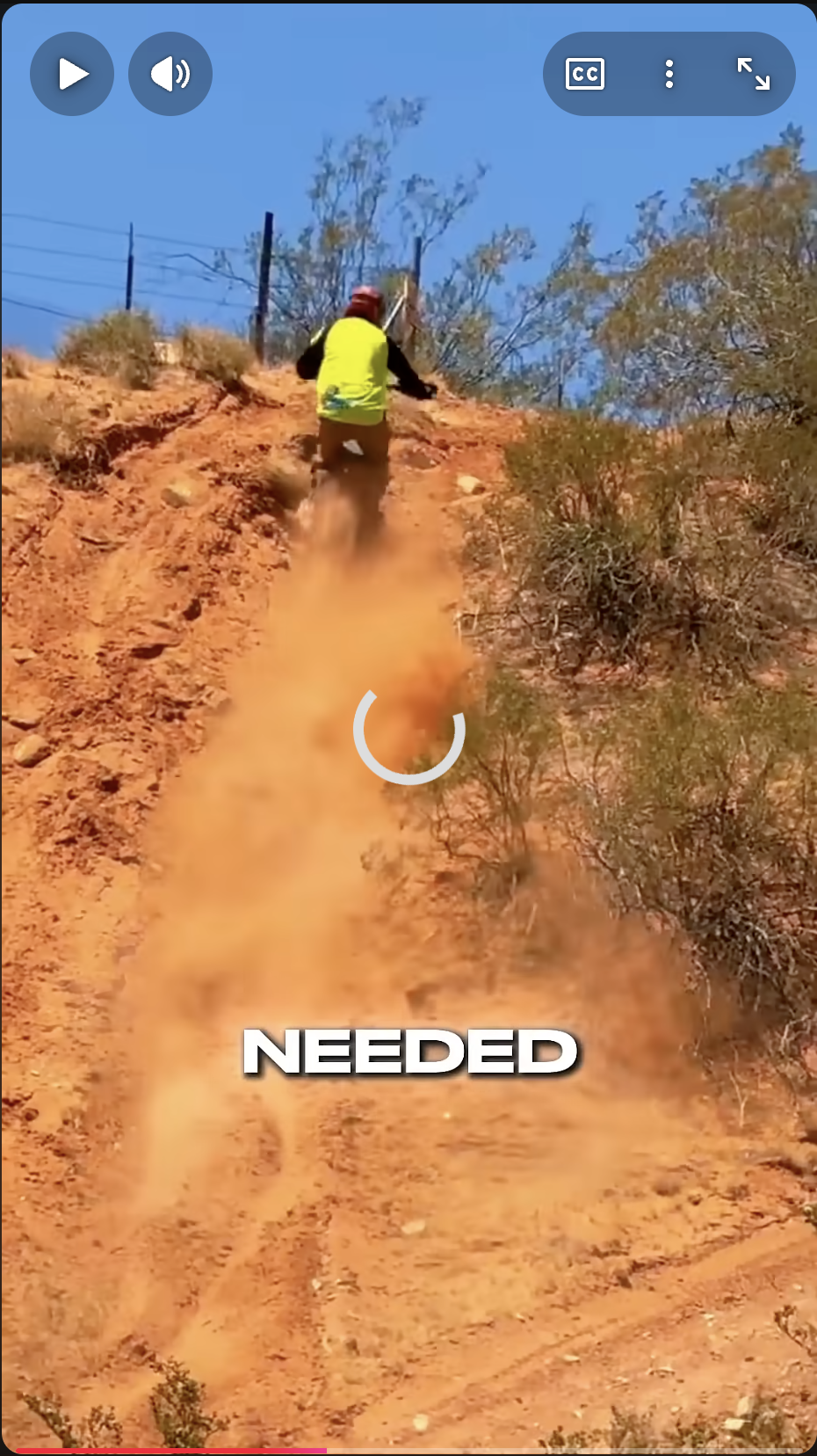 Person wearing yellow and red riding a dirt bike up a dusty hill with dust rising behind.