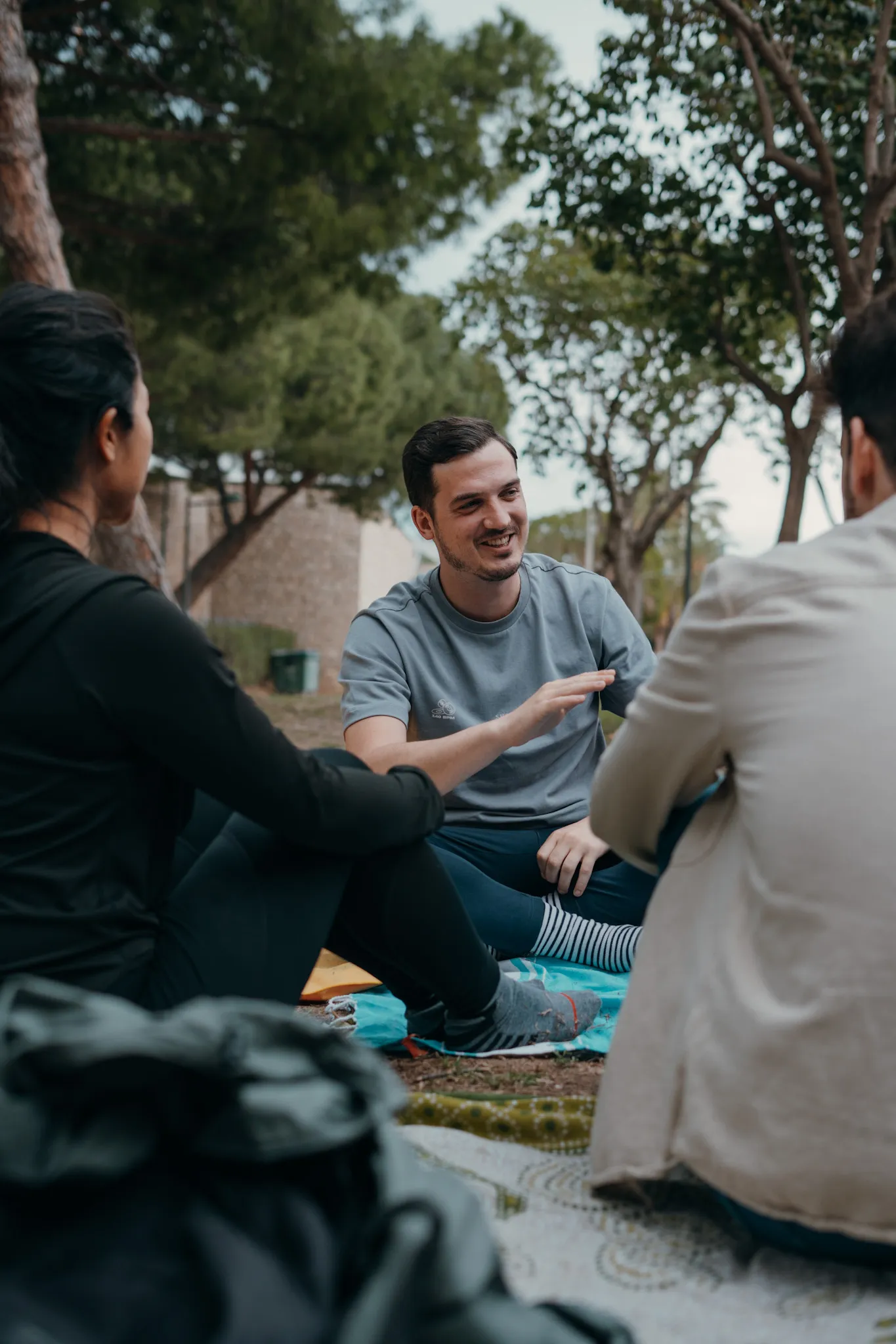 Three people sitting on blankets in a park, engaged in a friendly conversation.