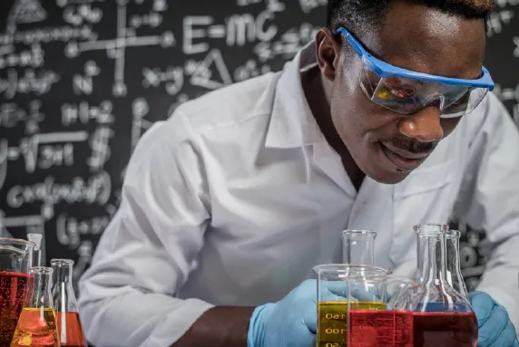 un homme en blouse de laboratoire et lunettes de protection travaillant avec des flacons.