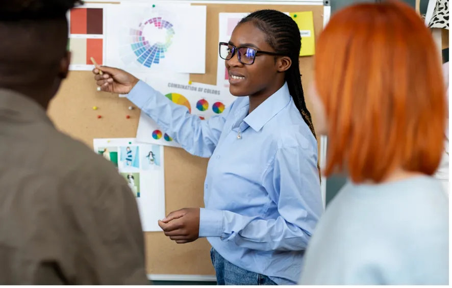 une femme à lunettes pointe vers un tableau.