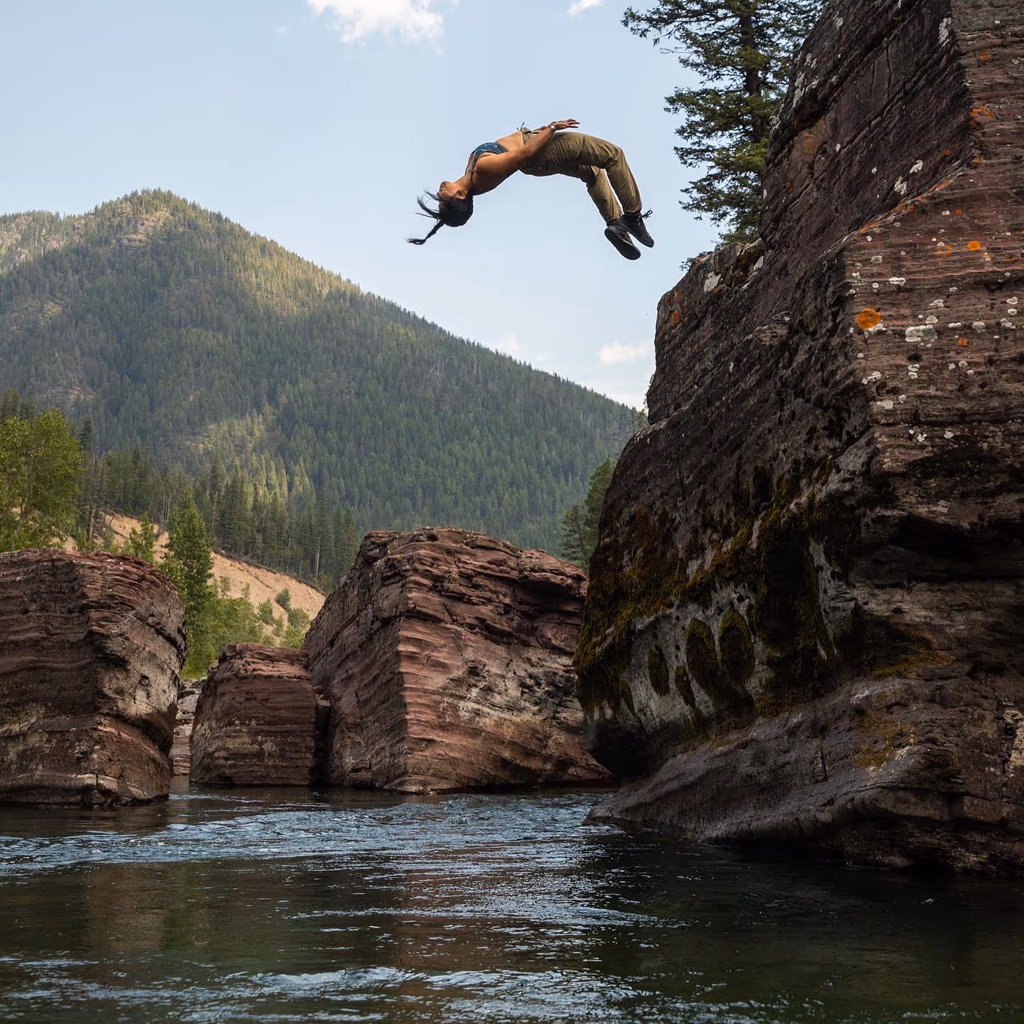 woman doing backflip off cliff into river