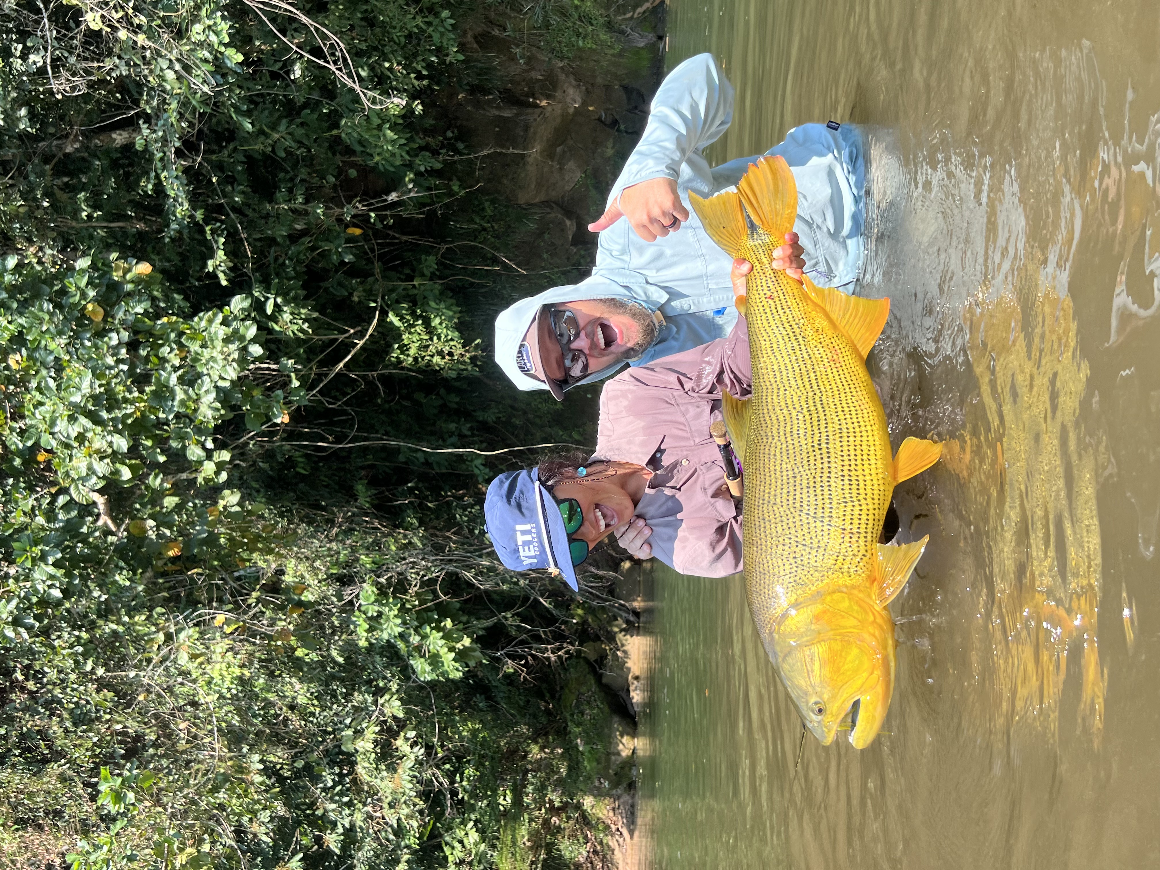 woman and man holding golden dorado fish in river