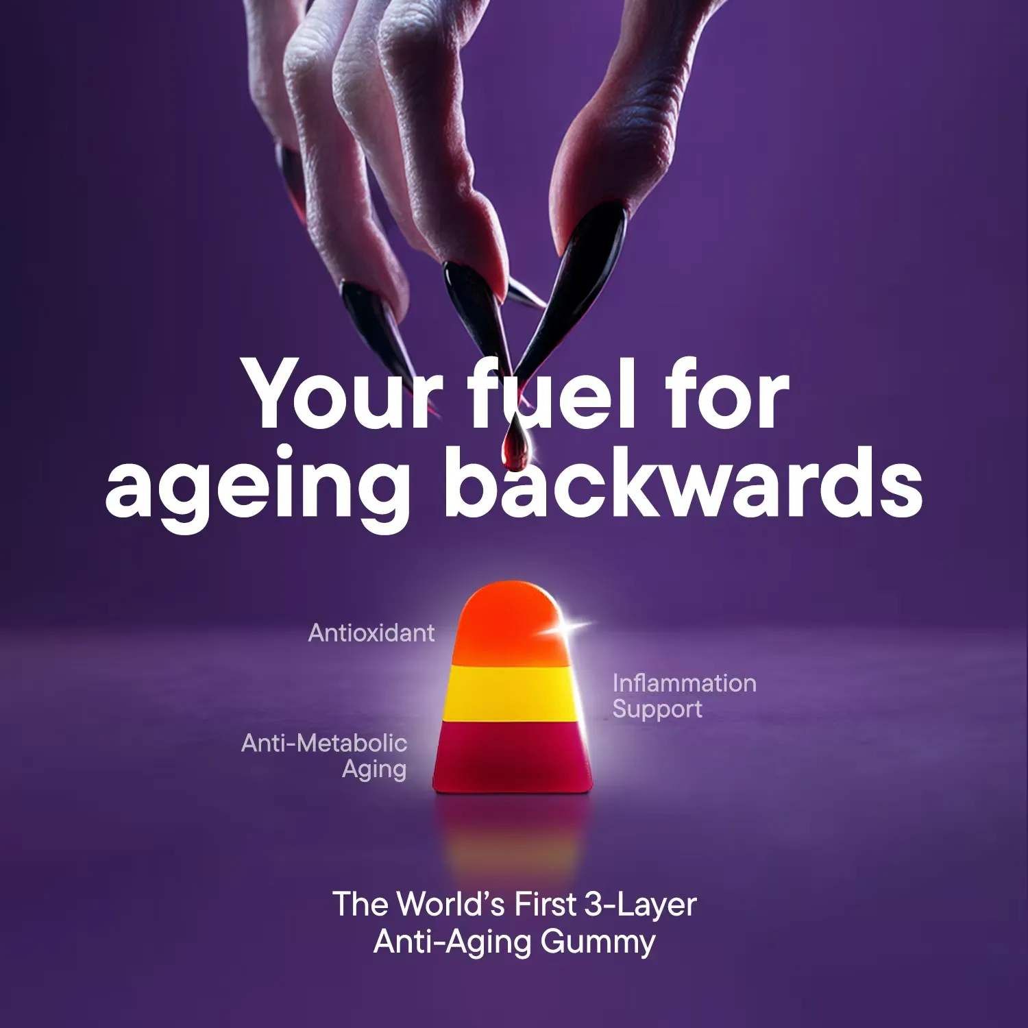 Hand with long black nails drops red liquid above a colorful 3-layer anti-aging gummy.
