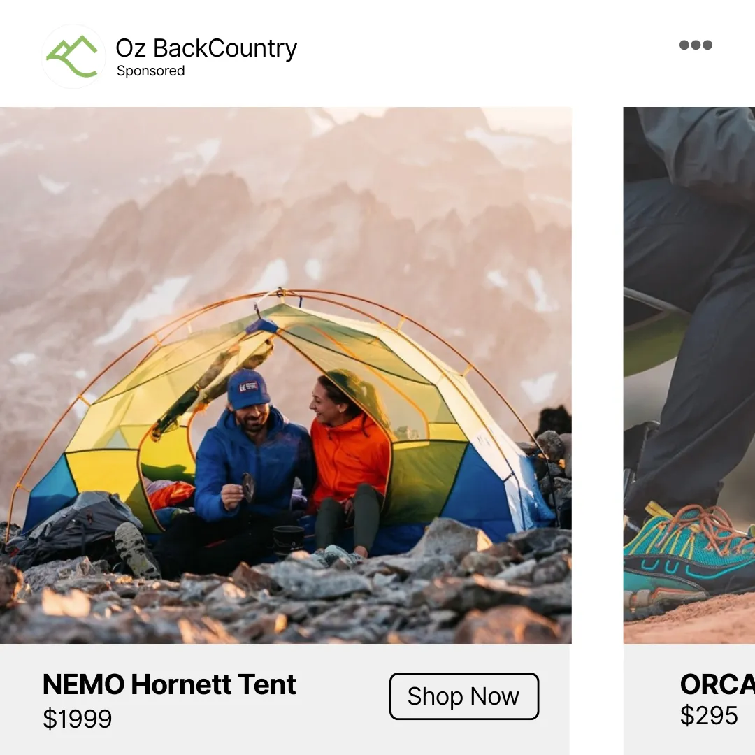 Two people sitting inside a yellow and blue tent on rocky terrain with mountains in background.