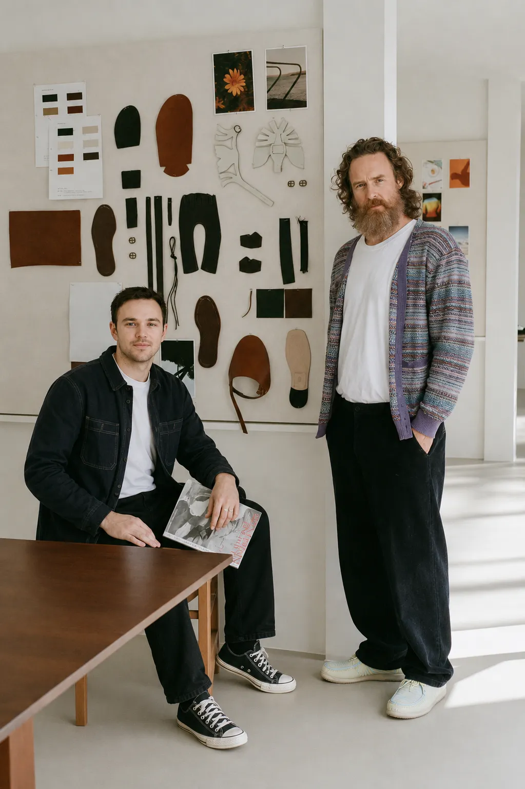 Two men in casual clothes in a design studio with shoe pattern pieces on the wall behind them.