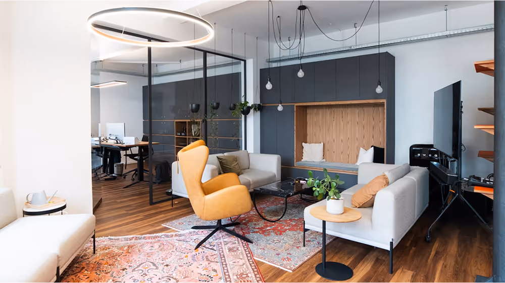Our Fürther office lounge with gray sofas, a yellow swivel chair, dark coffee table, and built-in wooden seating niche