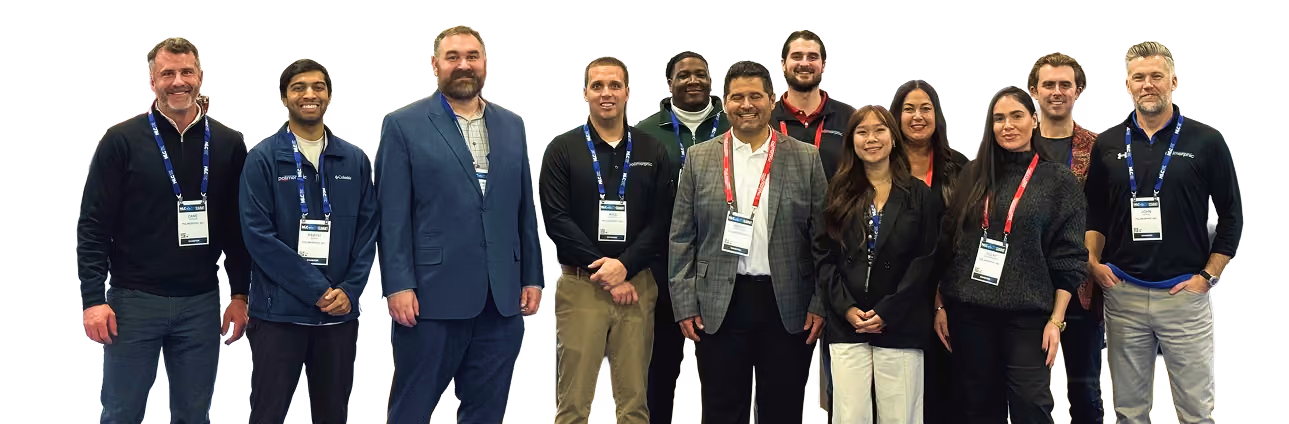 Smiling diverse team of eleven professionals standing in a row wearing badges and business casual attire.