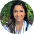 Smiling woman with long dark hair wearing a white shirt, posing outdoors with green foliage background.
