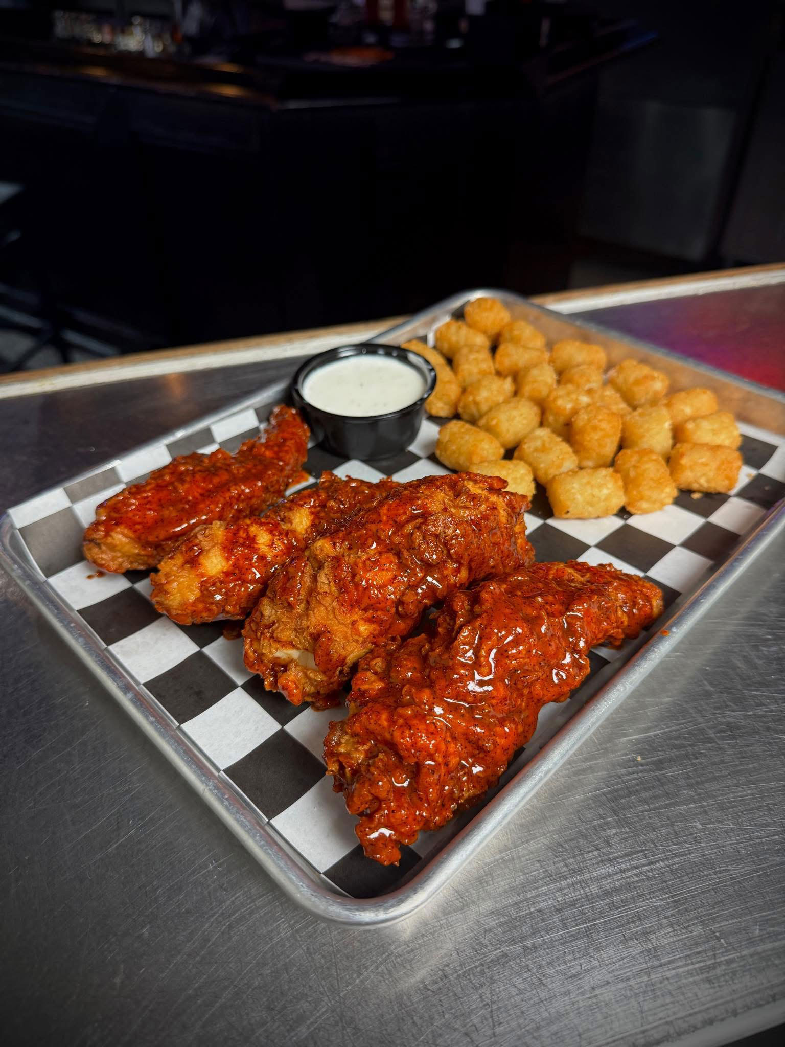 Trays of fried fish, popcorn shrimp, French fries, lemon wedges, and dipping sauces on a metal surface.