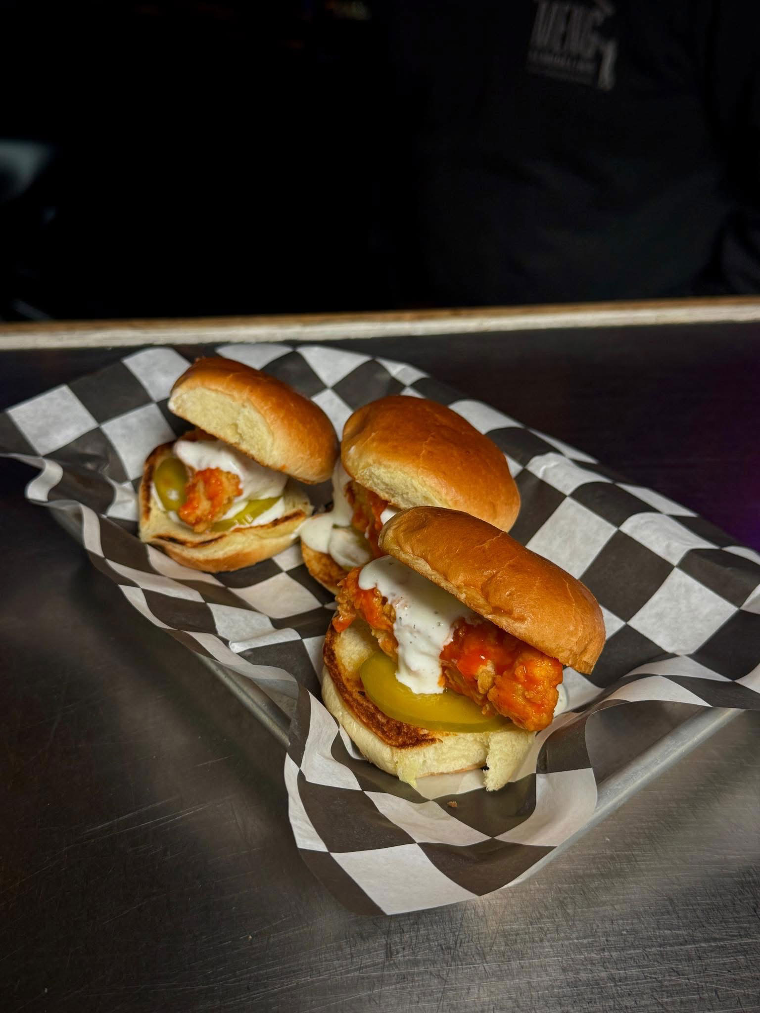 Two bacon cheeseburgers with melted cheese on toasted buns served on metal trays in a restaurant setting.