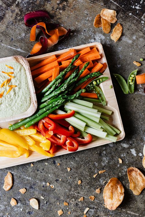 A colorful crudites tray with fresh hummus catered by DSquared Hospitality Company sits on a grey stone counter