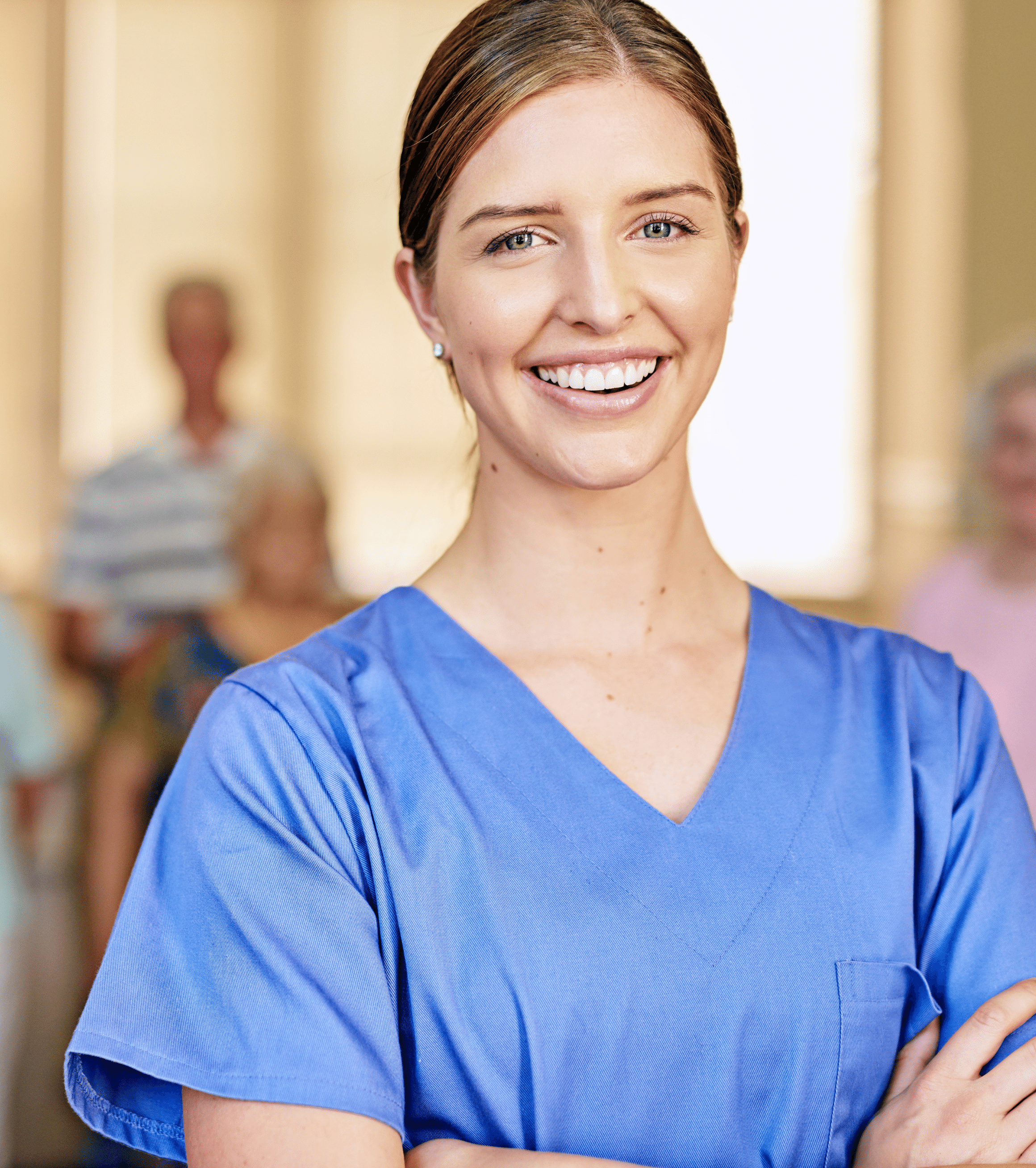 Portrait of a confident female caregiver in a blue uniform, smiling at the camera, with elderly residents visible in the soft-focused background, symbolizing dedicated and compassionate care.