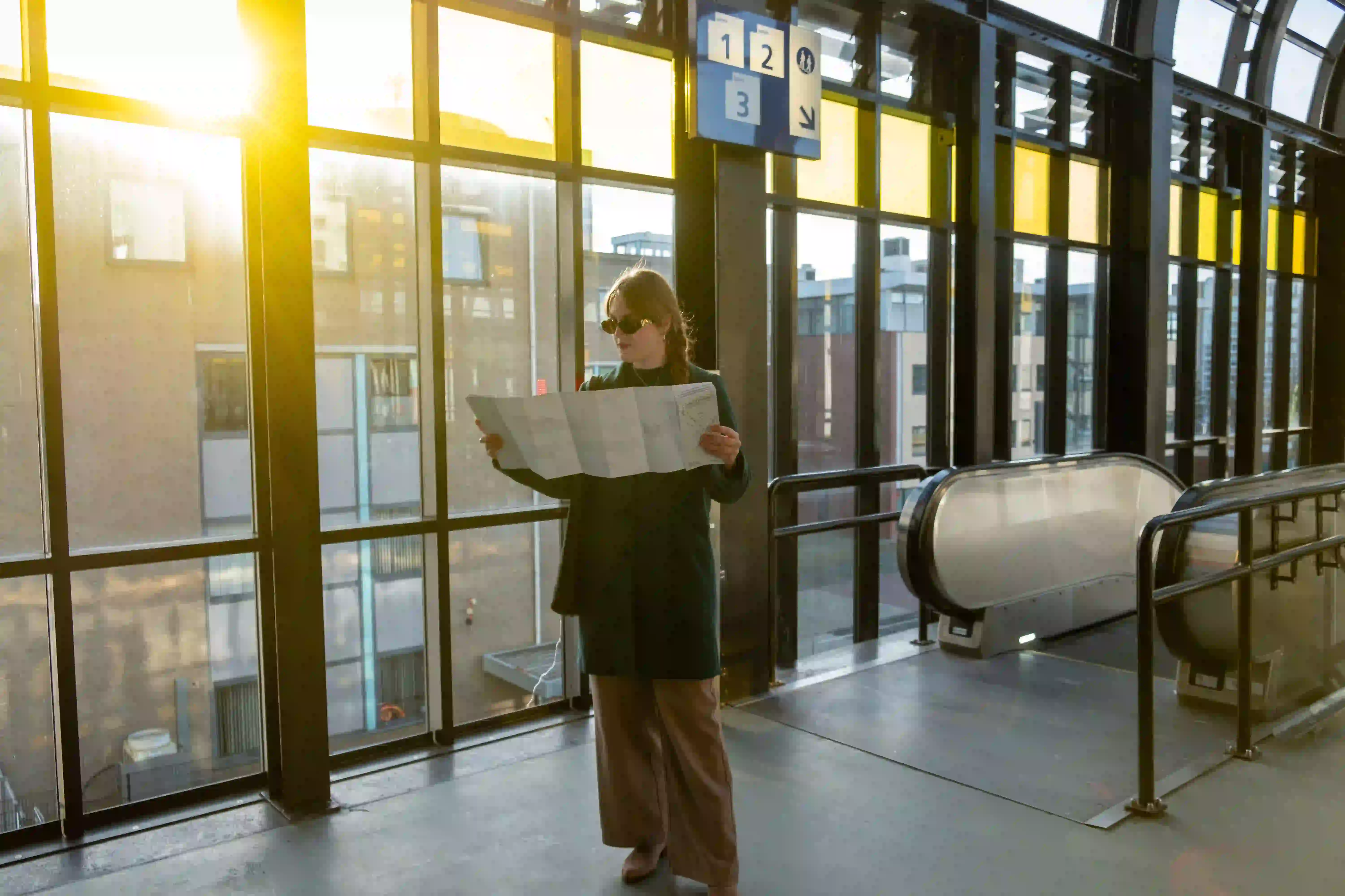 erson standing in a sunlit station holding and reading a large folded map.