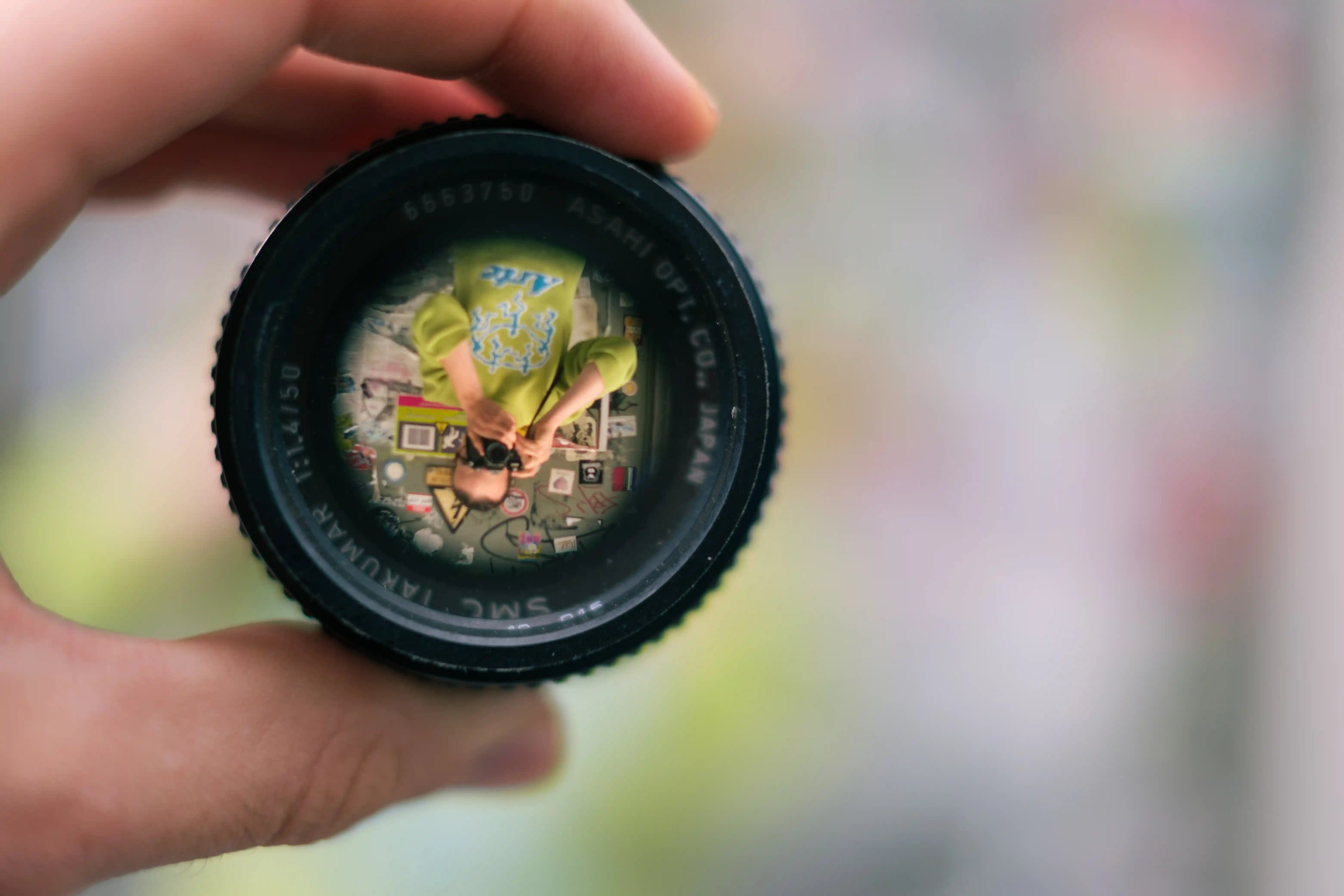 Hand holding a camera lens that frames a self-portrait reflected inside the glass.