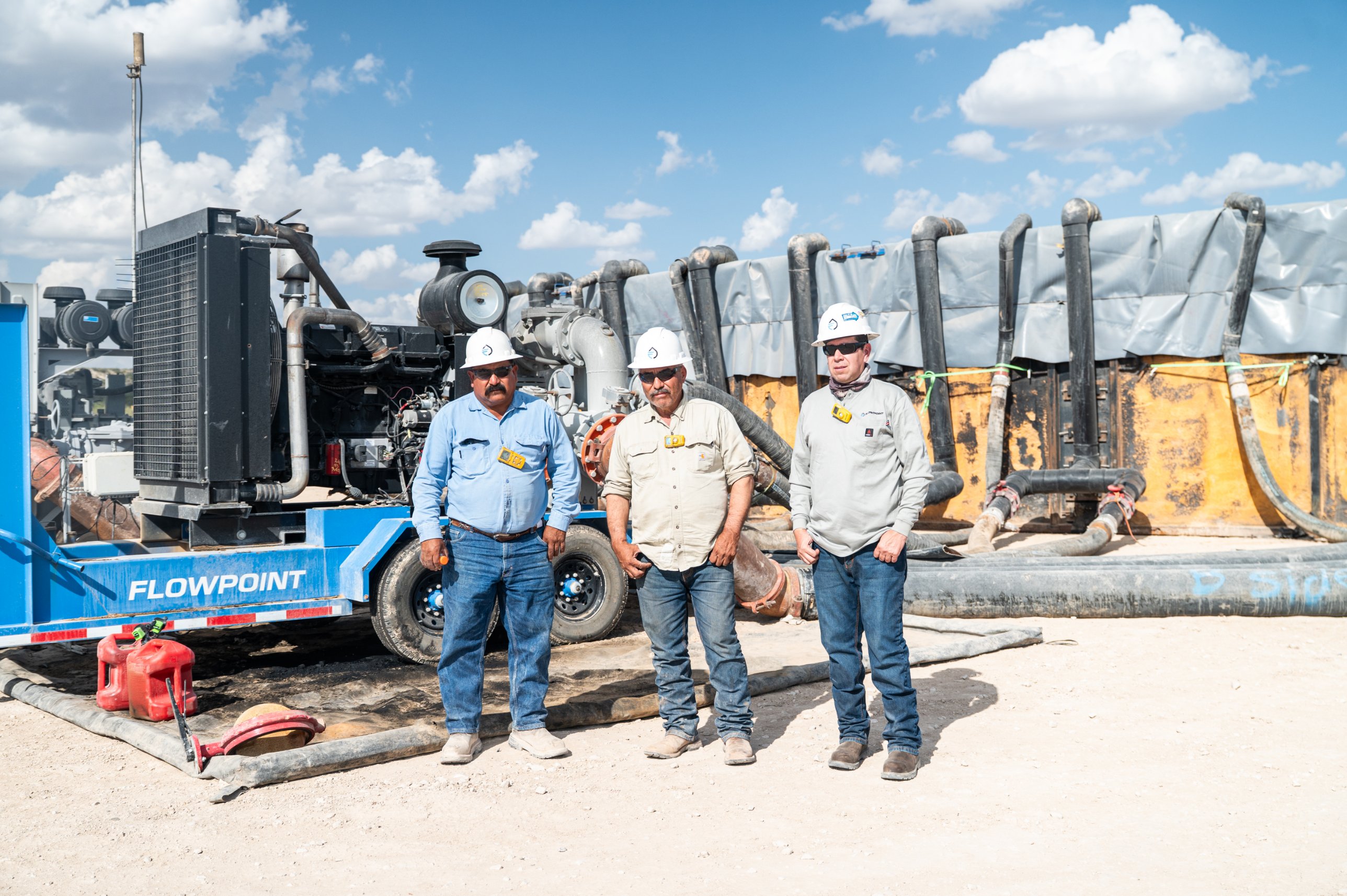 Flowpoint crew on location beside a Flowpoint pump trailer at a pit in the Permian Basin