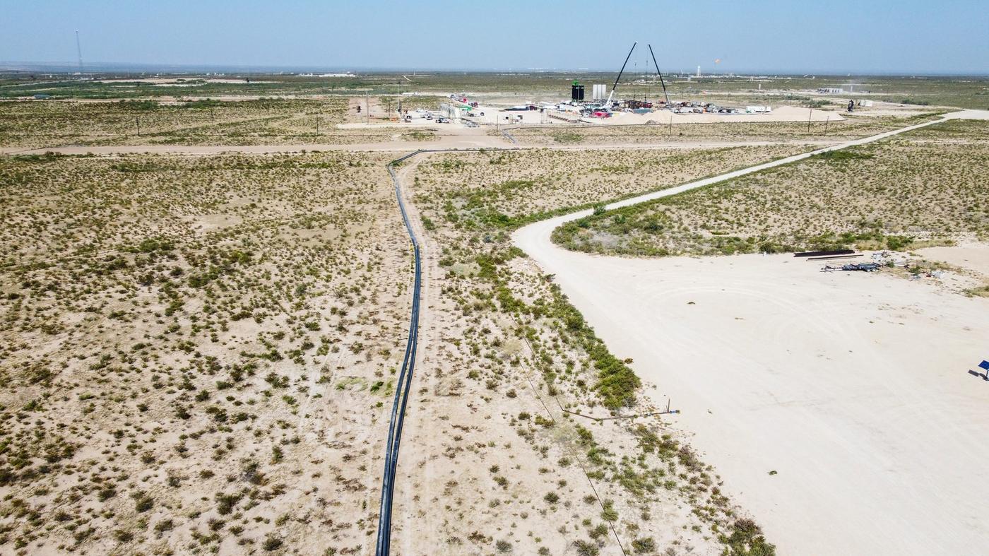 Water transfer line running across open West Texas country toward a rig