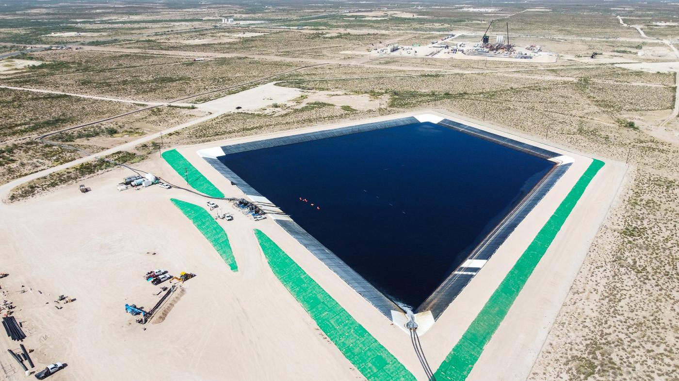 Wide aerial of a Flowpoint frac water pit with a drilling rig beyond