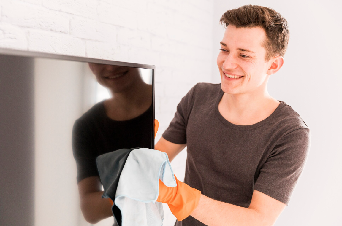 Young man smiling while cleaning a TV, representing skill-building and responsibility encouraged in Portland sober living environments