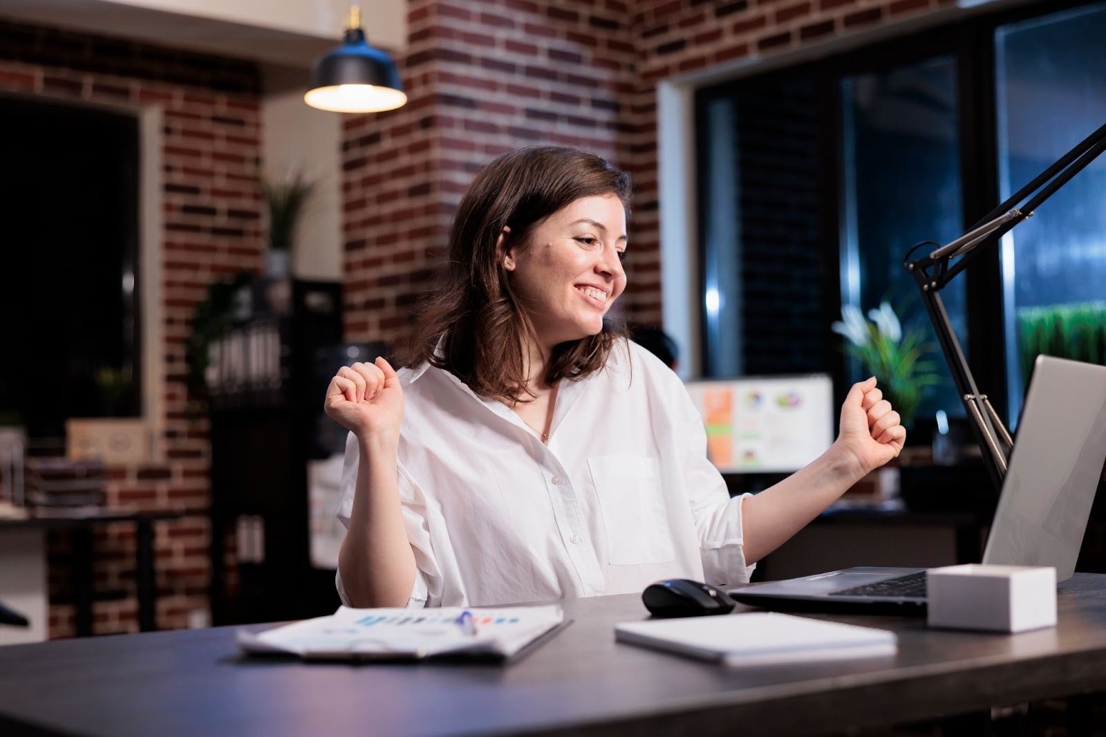 A happy woman smiling in front of a laptop and paperwork while sitting in a desk in a home office