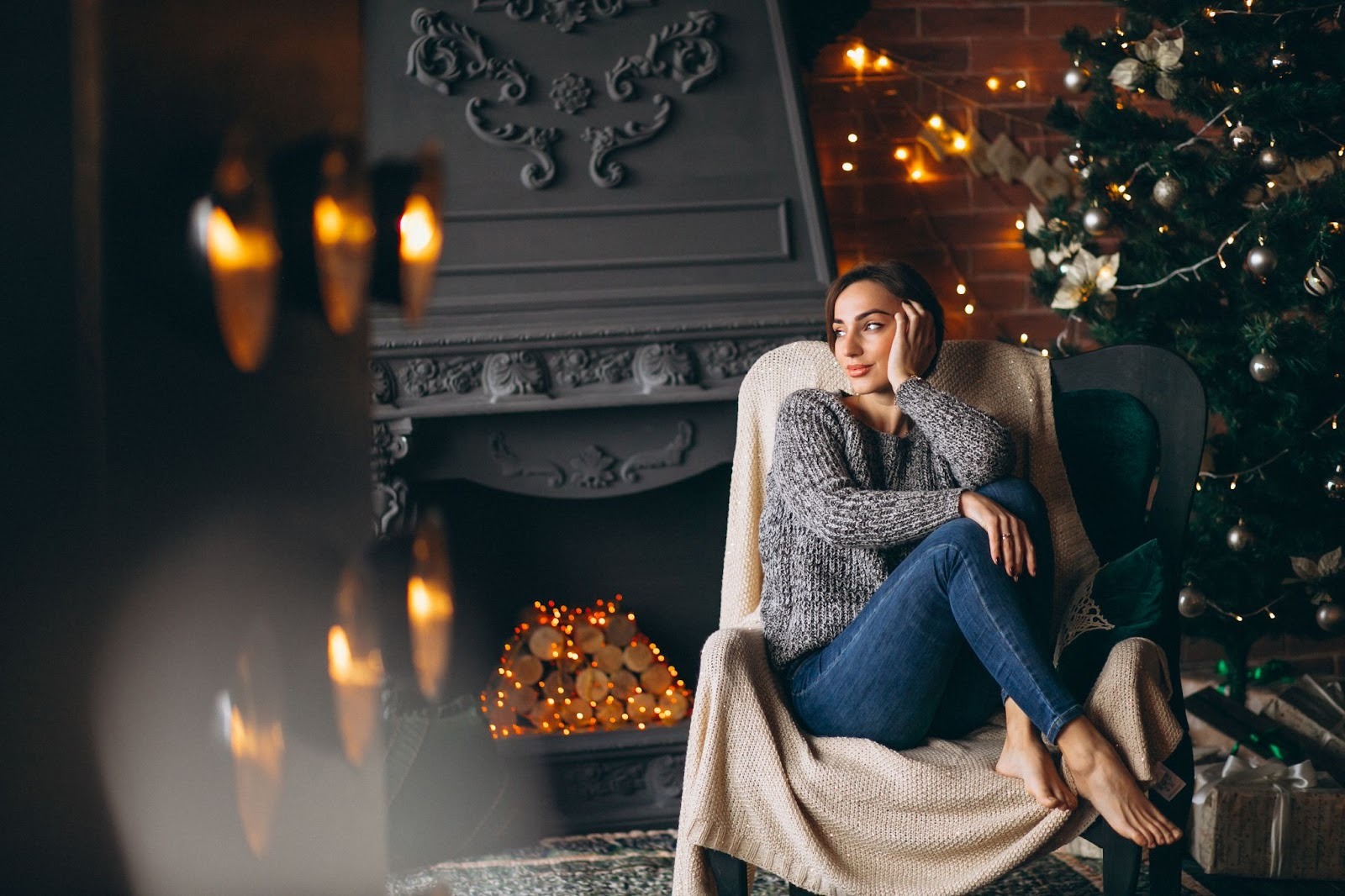 A woman cozily sitting by the fireplace and Christmas tree