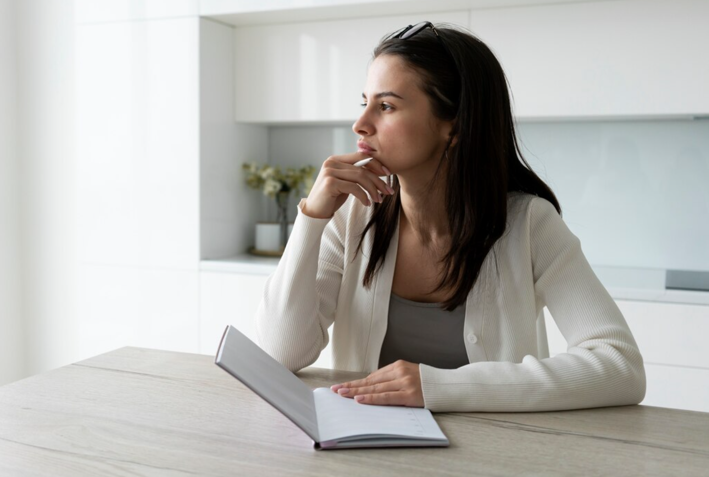 A woman sitting at a table, holding a pen and notebook, thinking about whether to choose HIOP or traditional rehab