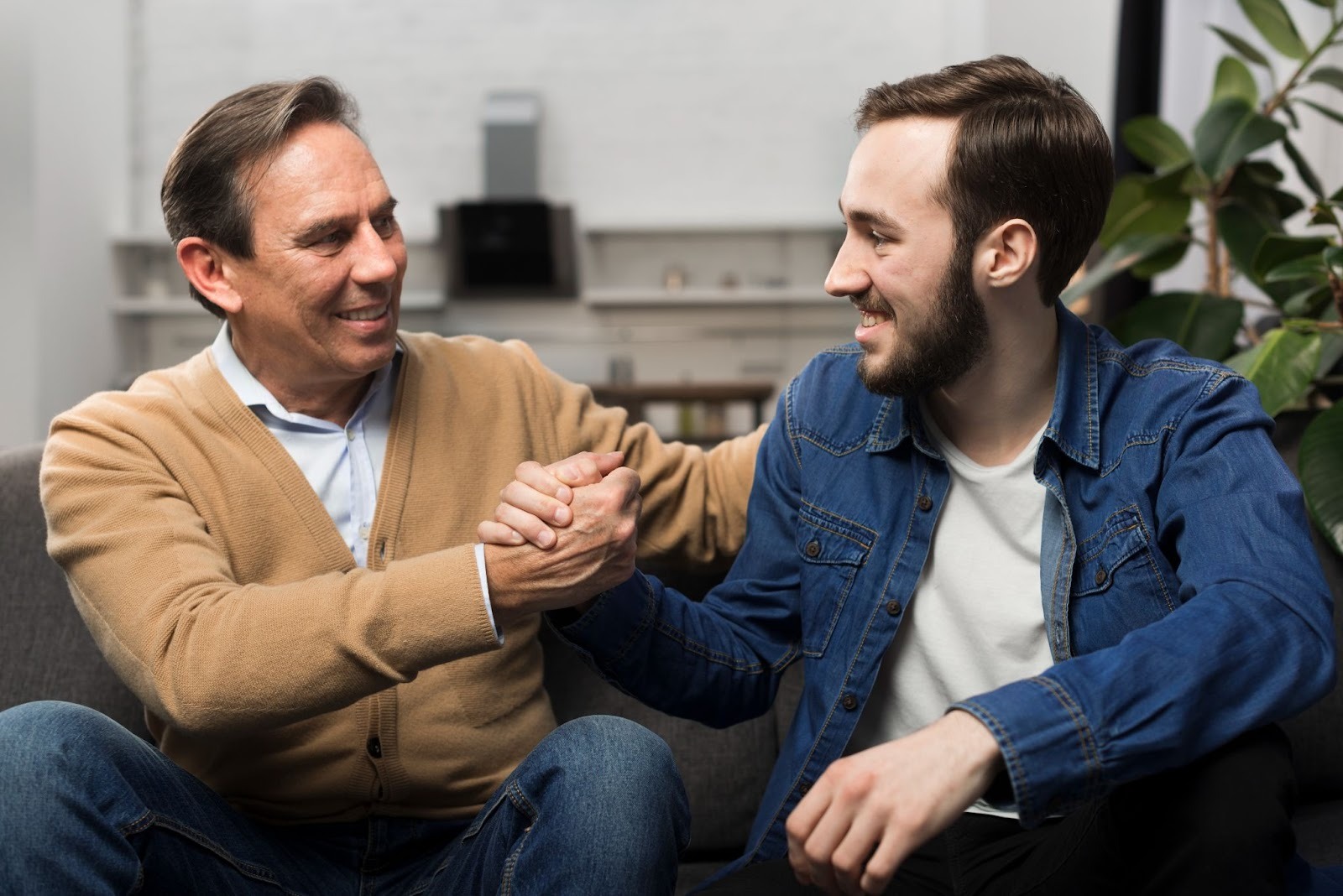 A father and son shaking hands while sitting on a chair, visibly contented with the results of outpatient drug and alcohol treatment 