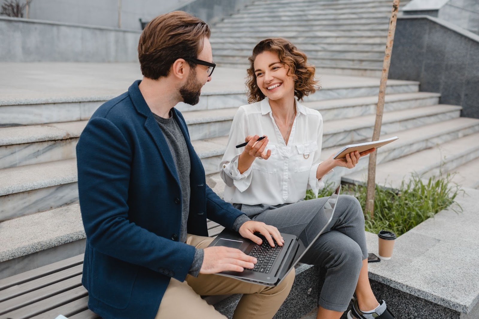 A man and woman sit on outdoor steps, smiling and engaged in conversation, representing supportive relationships and recovery guidance associated with a Partial Hospitalization Program