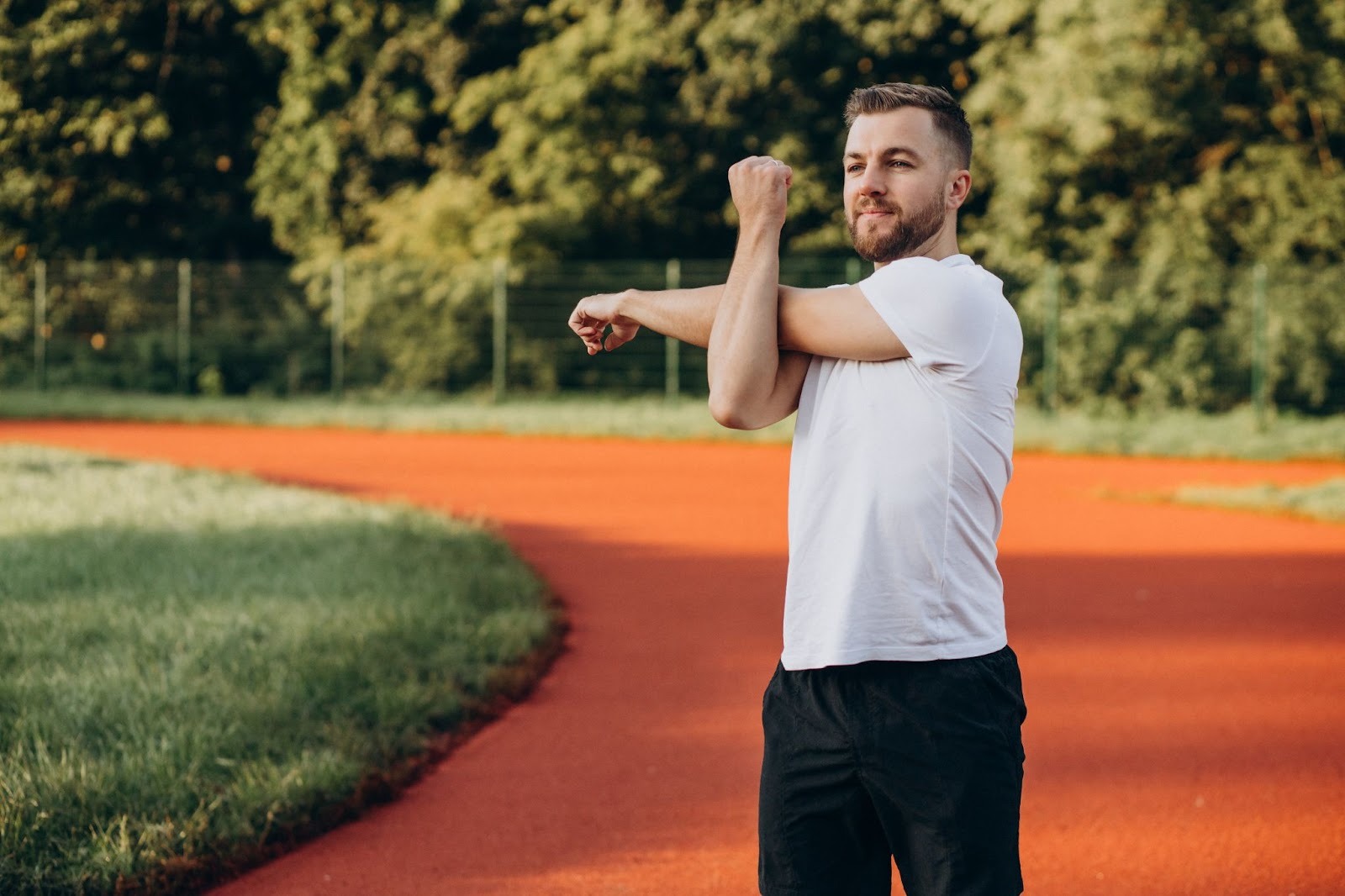 A man in a white shirt stretches on a red track, warming up and staying active to support his body’s natural detox from weed use