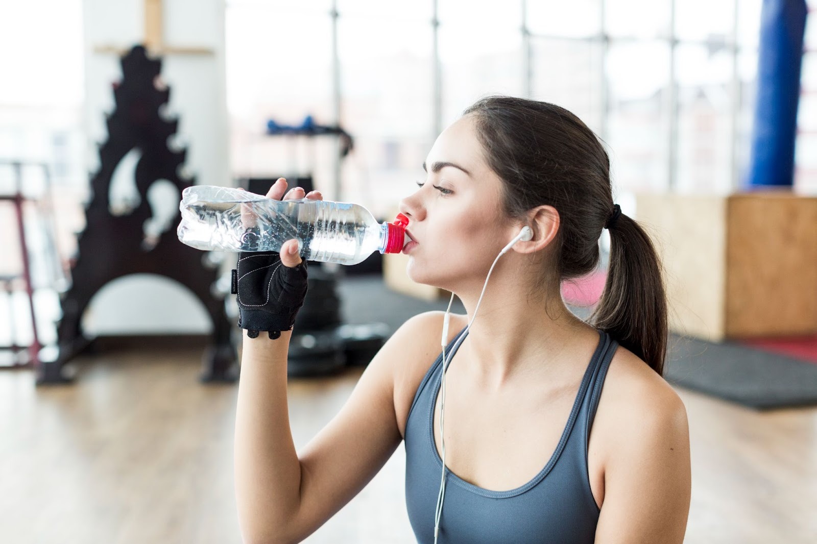 A woman in a gym drinks water after a workout, staying active and hydrated while trying to get weed out of her system