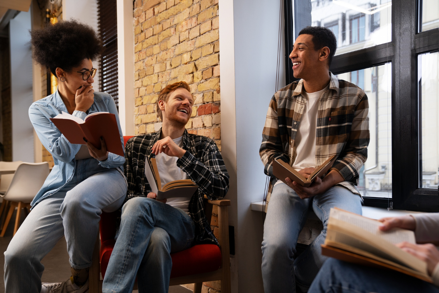 Group of young adults sitting together indoors, holding books and laughing during a casual discussion