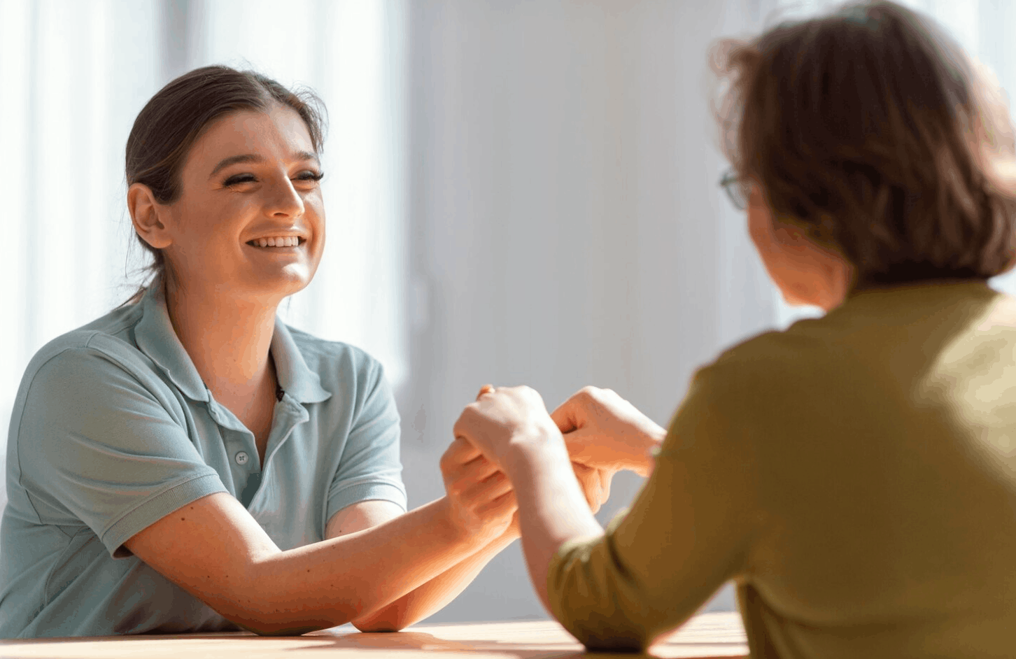 Two people sitting across from each other holding hands during a supportive conversation in a recovery setting