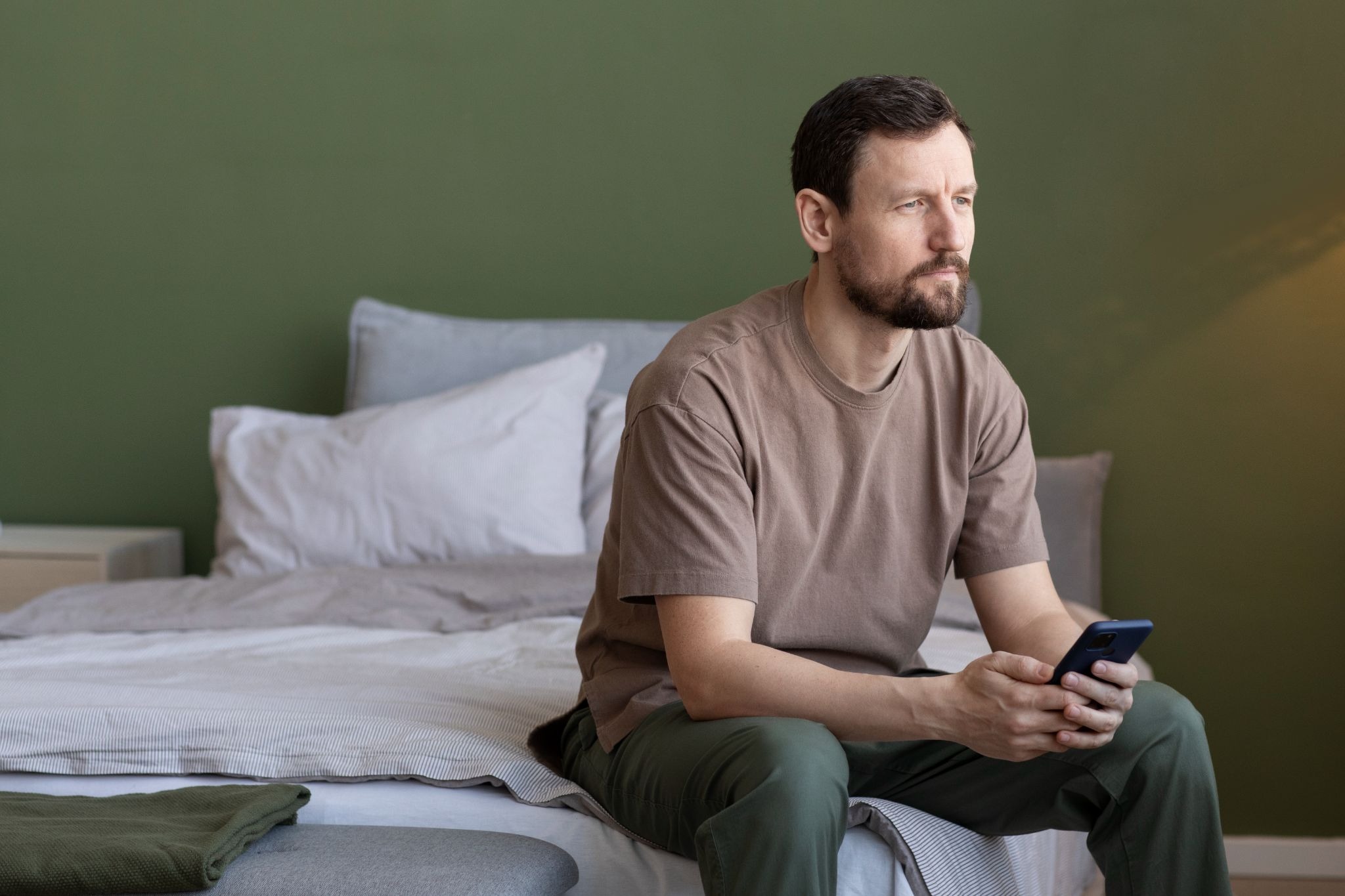 Man sitting on a bed holding a phone while reflecting on recovery and seeking support after relapse