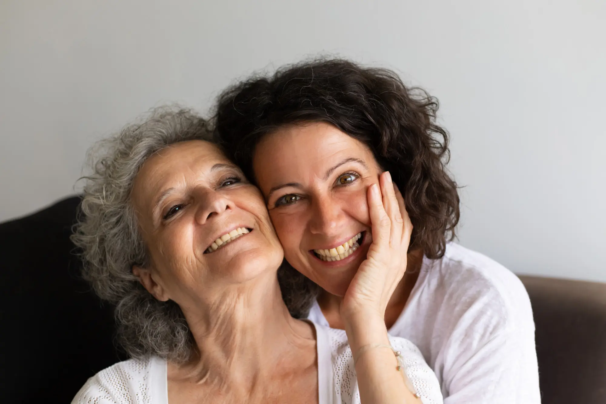 A smiling mother and adult daughter share a warm, supportive moment together.