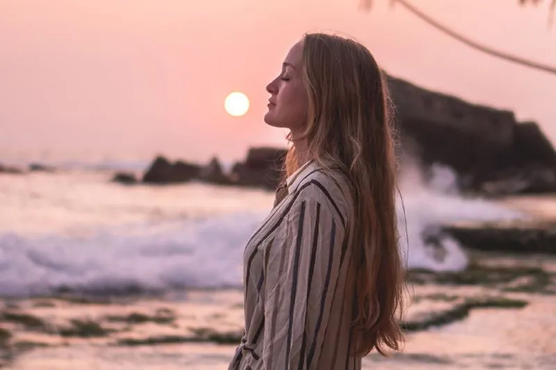 A woman with long hair and a striped shirt standing on the beach.