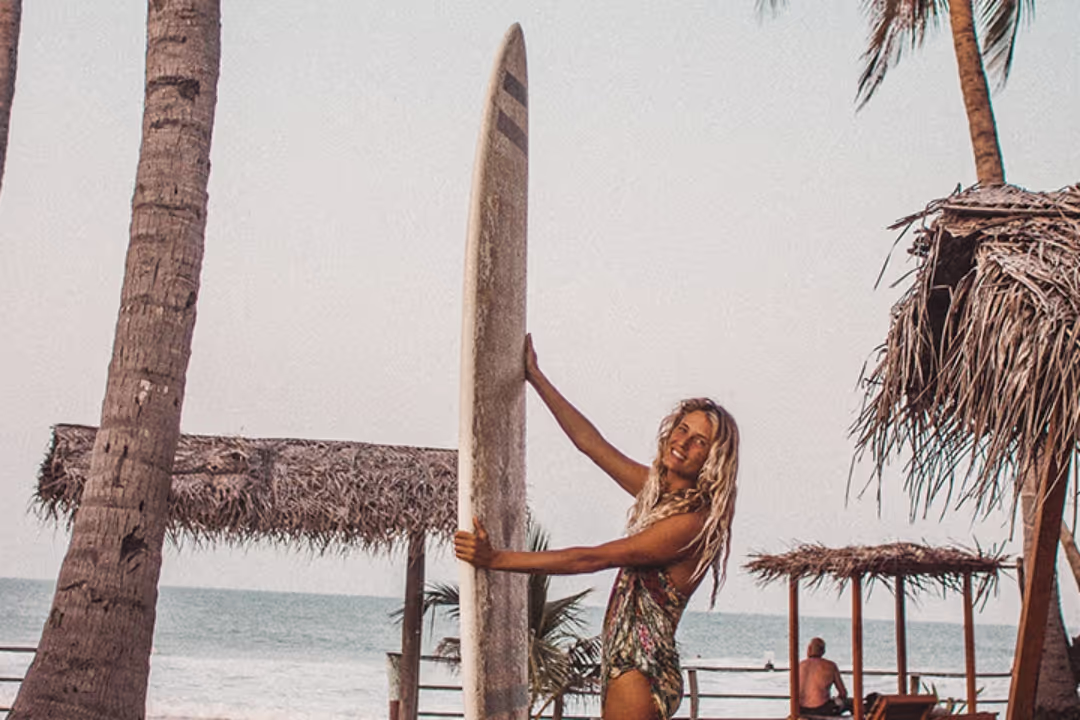 A woman holding a surfboard in front of a palm tree.