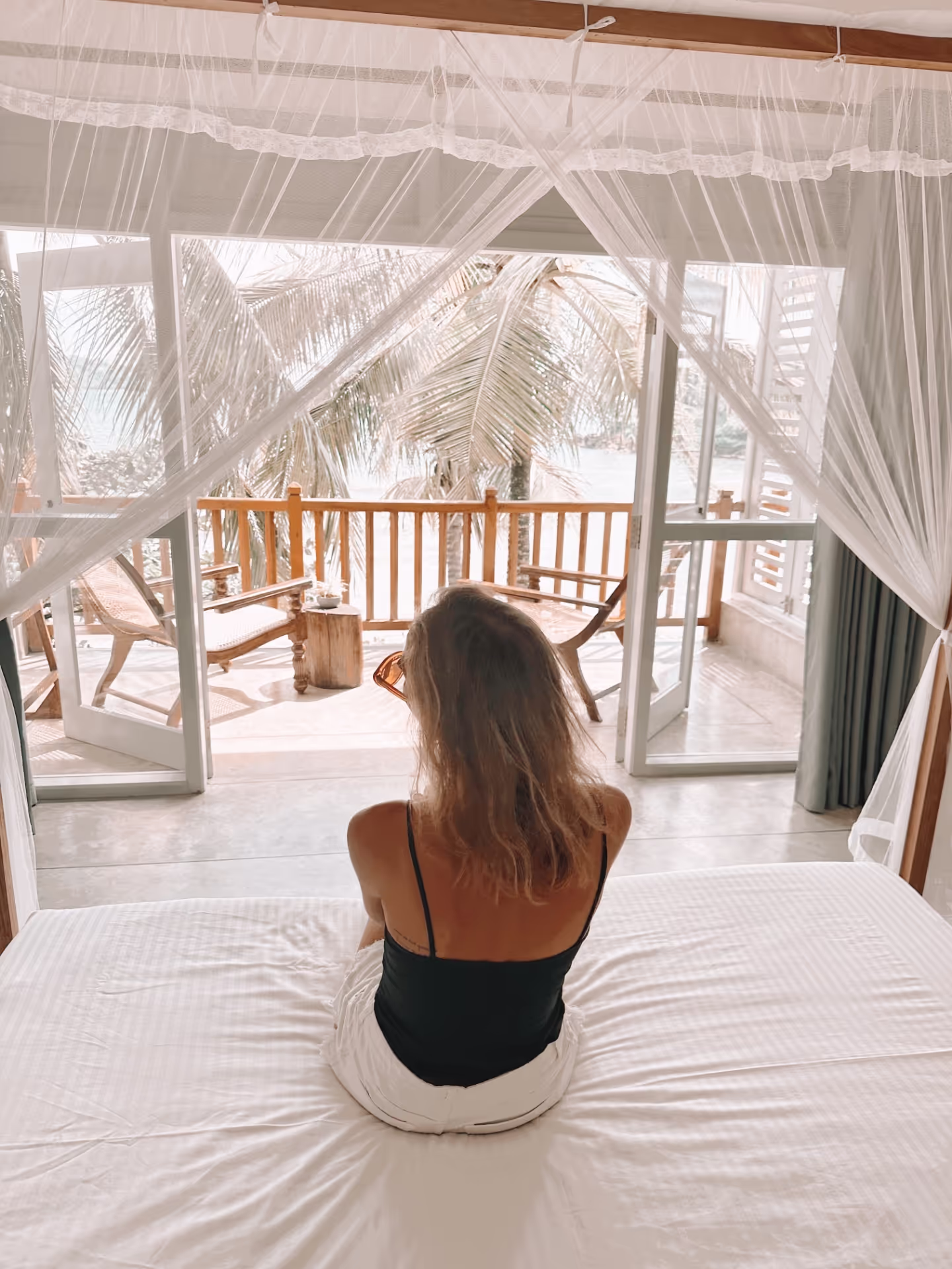 A woman sitting on a bed in a room with a view of the ocean.