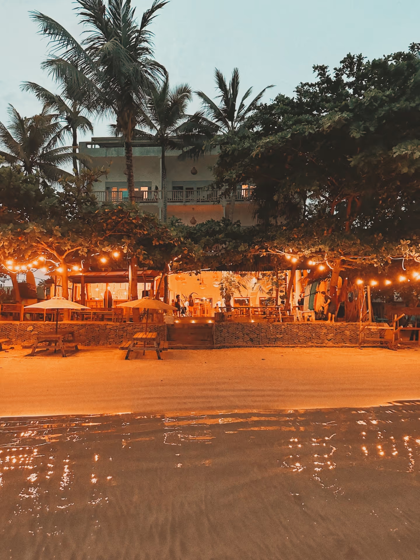 A beachside restaurant with a thatched roof and palm trees.