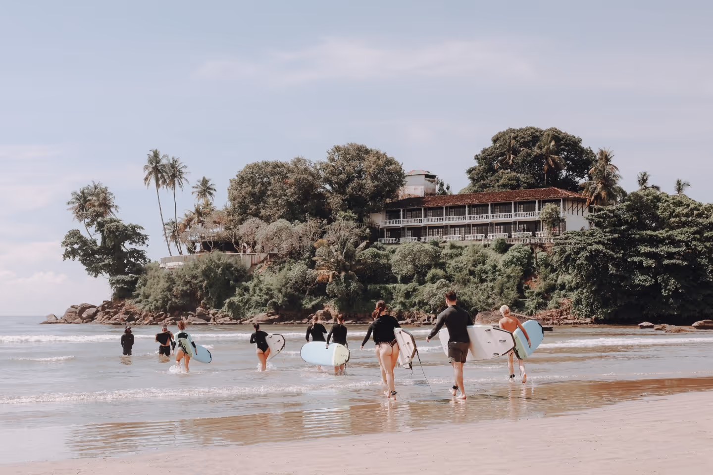 A group of people walking on the beach with surfboards.